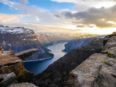 Téléchargez les photos : Famous rock formation, Trolltunga with a view from the above on Ringedalsvatnet lake, Norway. Rock hanging. Slopes of the mountains are partially covered with snow. Soft colors of the sunrise - en image libre de droit