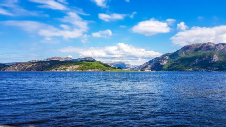 Téléchargez les photos : A wast fjord near Rogaland, Norway. Water of the fjord is slightly wavy. Bright sunbeams reflect in the water's surface. In the back tall mountains are shrouded in fog. - en image libre de droit