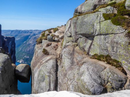 Foto de Una roca atrevida, Kjerag, Noruega. La roca en forma de bola está colgando entre dos paredes de piedra empinadas con una caída libre de 1000m. Detrás de ella está Lysefjorden. Día brillante y claro. - Imagen libre de derechos
