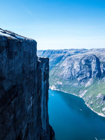 Foto de Una vista desde la cima de una montaña en el impresionante Lysefjorden brillando con muchos tonos de azul y verde. Pendientes empinadas de la montaña, cascada corriendo por las empinadas laderas. Pendientes duras y estériles. - Imagen libre de derechos