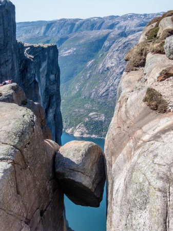 Foto de Una roca atrevida, Kjerag, Noruega. La roca en forma de bola está colgando entre dos paredes de piedra empinadas con una caída libre de 1000m. Detrás de ella está Lysefjorden. Día brillante y claro. - Imagen libre de derechos