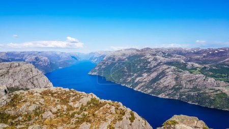 Photo for A stunning view on Lysefjorden from Preikestolen. Surface of the water located 600m below. A ship moving through it.  Steep cliffs are joining the water on both sides. A bit of mist in the back. - Royalty Free Image