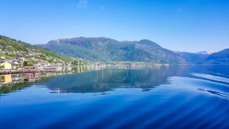 Téléchargez les photos : A view on the Songefjorden (King of the Fjords) from the water level. It is the deepest fjord in Norway. Tall, lush green mountains surrounding the fjord. Wavy surface of the water. Clear blue sky. - en image libre de droit