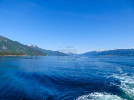 Téléchargez les photos : A view on the Songefjorden (King of the Fjords) from the water level. It is the deepest fjord in Norway. Tall, lush green mountains surrounding the fjord. Wavy surface of the water. Clear blue sky. - en image libre de droit