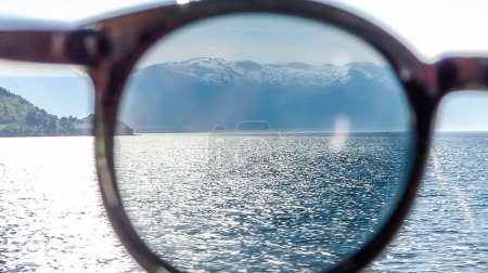 Téléchargez les photos : A view on the Songefjorden (King of the Fjords) from the water level through sunglasses. Tall, lush green mountains surrounding the fjord. Calm surface of the water. Clear blue sky. - en image libre de droit