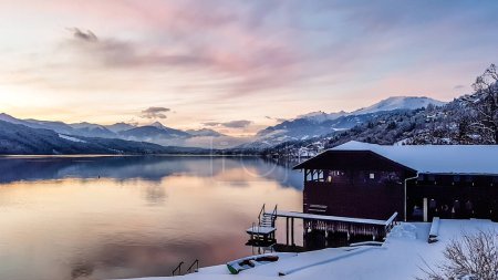 Photo for Beautiful view on Millstaetter lake in Austria. The lake is surrounded by Alps. Mountains are covered with snow. The sky is exploding with pink and orange. Stunning sunset. Little cottage on the side. - Royalty Free Image