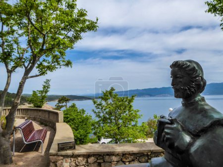 Téléchargez les photos : Vrbnik / Croatie-05 / 01 / 2018 : Statue d'un homme, située au sommet d'une colline avec une belle vue sur la mer. Quelques arbres perturbant la vue sur la mer. Banc avec vue sur la mer. - en image libre de droit
