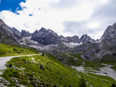 Téléchargez les photos : Route étroite en gravier menant à la chaîne de montagnes pierreuses de Lienz Dolomites, Autriche. Les montagnes sont partiellement envahies par des buissons. Dangereux alpinisme. Grands arbres poussant devant - en image libre de droit