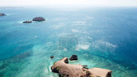Foto de Hermosas formaciones de promontorios en Lombok, Indonesia. Barcos aparcados en las orillas de la Playa Rosa, aguas cristalinas, que brillan con tonos azules. Captura de drones. Gema oculta, virgen. - Imagen libre de derechos