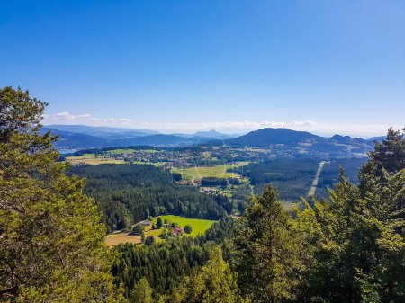 Photo for A panoramic, areal view on an alpine landscape of Austria. There are high Alps in the back. Few trees on the side, forming a small forest. Idyllic landscape. There is a tower on one of the mountains. - Royalty Free Image