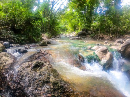 Foto de Una fuente termal que se fusiona con un río frío creando una temperatura perfecta de agua para nadar en Bajawa, Flores, Indonesia. Las orillas del río están cubiertas de árboles. Un montón de musgo en el fondo - Imagen libre de derechos