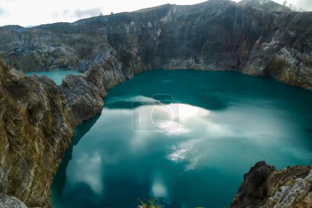 Foto de Vista de cerca de los lagos del cráter volcánico Kelimutu en Flores Indonesia. Los lagos están brillando con muchos tonos de turquesa y azul. El sol brilla entre las nubes. Pendientes áridas y agudas del cráter volcánico - Imagen libre de derechos