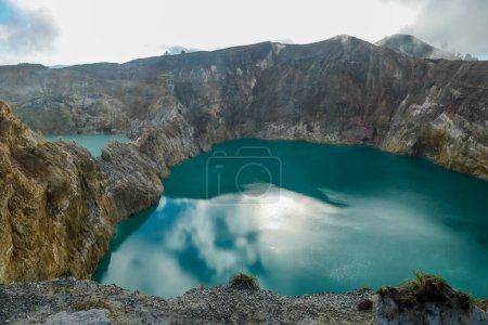 Foto de Vista de los lagos del cráter volcánico Kelimutu en Flores, Indonesia. Los lagos están brillando con muchos tonos de turquesa y azul. El sol brilla entre las nubes. Pendientes áridas y agudas del cráter volcánico - Imagen libre de derechos