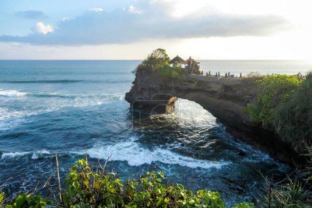 Klippen in der Nähe des Tanah Lot Tempels, Bali, Indonesien. Es gibt einen Bogen im Wasser. Die Wellen plätschern an den Klippen und kleineren Felsen. Wasser bleibt auf den flachen Oberflächen. Die Kraft der Natur
