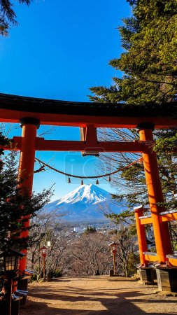 Photo for Distant view on Mt Fuji, framed in between orange Torri gate, leading to Chureito Pagoda in Japan, on a clear, wintery day. The top parts of the volcano are covered with a layer of snow. Holly mountain - Royalty Free Image