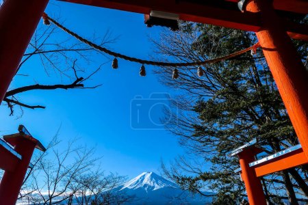 Photo for Distant view on Mt Fuji, framed in between orange Torri gate, leading to Chureito Pagoda in Japan, on a clear, wintery day. The top parts of the volcano are covered with a layer of snow. Holly mountain - Royalty Free Image
