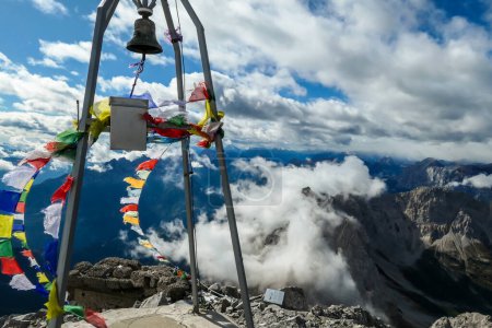 Photo for View from the top of Monte Coglians, Hohe Warte on the Austrian-Italian Alpine border. Metal construction with a bell, wrapped with prayer flags waving on the wind. Happiness and achievement. Overcast - Royalty Free Image