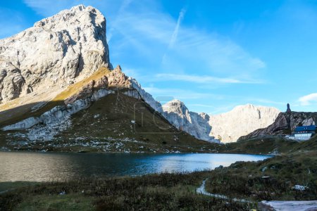 Photo for Panoramic shot of a soft reflection of an Alpine mountain in Wolayer Lake Austria. There is a mountain cottage at the shore. Mountain is catching the first sunbeams. Peace of mind, calmness. - Royalty Free Image