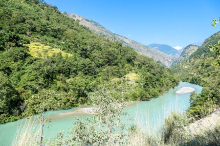 Foto de A panoramic view on river and Himalayas from Annapurna Circuit Trek, Nepal. Turquoise color of the river, big stones popping out of the river. Green forest around. Idyllic landscape. - Imagen libre de derechos