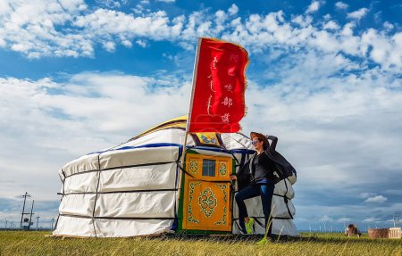 Foto de Xilinhot, Inner Mongolia/China - 07 20 2017: Girl with cow boy hat standing in front of a tent in inner Mongolia in China. Wind waves the flag above the yurt. - Imagen libre de derechos