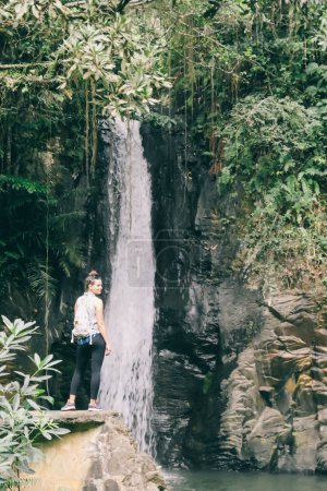 Foto de Una niña está admirando la cascada de Murukeba en el pequeño pueblo de Moni, isla de Flores, Indonesia. La selva tropical circundante crea una atmósfera mágica de inspiración y dedicación. - Imagen libre de derechos