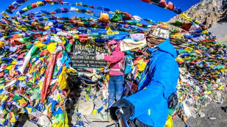 Téléchargez les photos : Couple, man and woman at the Thorung La Pass, Annapurna Circuit Trek, Nepal. Congratulations for the effort. Colorful Prayer flags attached to the stone wall, blow by the wind. Clear sky. - en image libre de droit