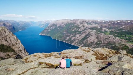 Paar sitzt auf einem Felsen und bewundert die Aussicht auf den Lysefjord. Flächenaufnahme, obere Perspektive auf das Paar. Endlose Aussicht auf den Fjord. Paar abseits der ausgetretenen Pfade, Freiheit beim Wandern.