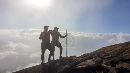 Foto de Una pareja con palos caminando al lado del volcán Inerie en Bajawa, Flores, Indonesia. Están rodeados de nubes, como si caminaran sobre ellas. Cielo azul claro. Fenómeno natural. Felicidad - Imagen libre de derechos