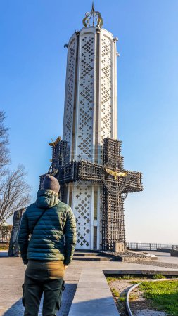 Téléchargez les photos : A young man admiring a candle-like tower, being part of Kiev Pechersk Lavra complex. Tower looks like a lit candle, surrounded by crosses from each side. Clear and sunny day. - en image libre de droit