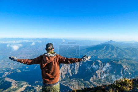 Foto de Un hombre de pie en la cima del volcán Inerie en Bajawa, Flores, Indonesia. Está disfrutando de la hermosa vista de la isla volcánica. Él extiende sus manos en un gesto de libertad. Nubes a su alrededor - Imagen libre de derechos