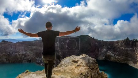 Foto de Hombre de pie en el borde del volcán con los brazos extendidos y observando los lagos del cráter volcánico Kelimutu en Moni, Flores, Indonesia. El hombre se involucra con la vida y tiene el sentimiento de libertad - Imagen libre de derechos