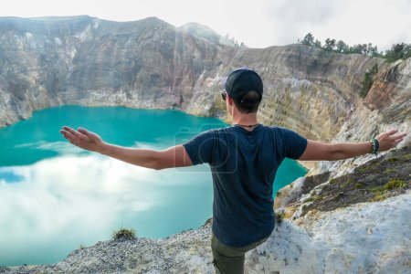 Foto de Hombre de pie en el borde del volcán con los brazos extendidos y observando los lagos del cráter volcánico Kelimutu en Moni, Flores, Indonesia. El hombre se involucra con la vida y tiene el sentimiento de libertad - Imagen libre de derechos
