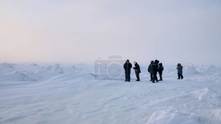 Téléchargez les photos : Vue grand angle d'un petit groupe de touristes dans un paysage arctique gelé, debout au milieu de monticules de neige et de formations de glace. - en image libre de droit