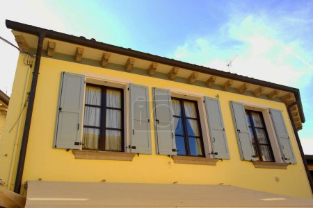 Façade latérale d'une maison jaune avec trois fenêtres