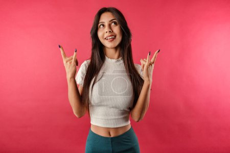 Foto de Portrait of cheerful woman wearing casual top isolated over red background crazy expression doing rock symbol with hands up. Looking upward. - Imagen libre de derechos