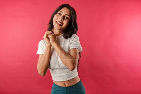 Foto de Young dark-haired girl smiling happy wearing ribbed crop isolated over red background puts hands together, looks at the camera with love, at you, and smiles. Very satisfied and happy. - Imagen libre de derechos