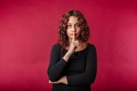 Photo for Young beautiful woman wearing black ribbed dress isolated over red background asking to be quiet with finger on lips. Silence and secret seriousness concept. - Royalty Free Image