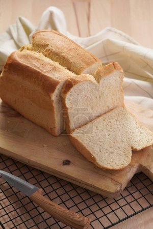 One freshly baked loaf of white wheat bread and cut slices on wooden board