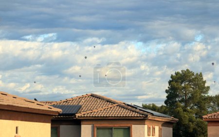 Photo for Hot-air balloons free flying high above house roofs and pine trees in a cloudy sky, Phoenix, Arizona in winter - Royalty Free Image