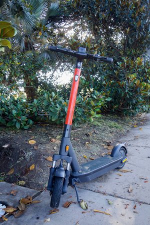 Téléchargez les photos : Dockless stand-up scooter électrique sur un pied stand sur un trottoir piétonnier à l'ombre des arbres - en image libre de droit
