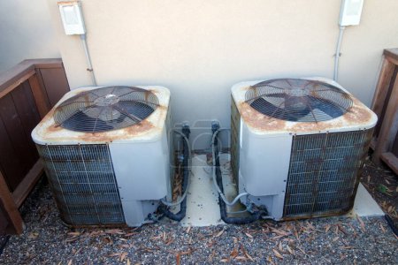 Rusty air conditioner outdoor units set next to backyard facing house wall