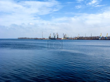 Dnieper reservoir north of DniproHES dam with distant cargo port cranes painted in yellow and blue colors of Ukrainian state flag, Zaporizhzhia, UA