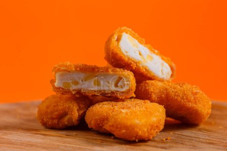 Crispy fried macaroni and cheese bites on a wooden board. Studio shot with orange background. Comfort food and snack concept. Design for menu, poster, and banner.