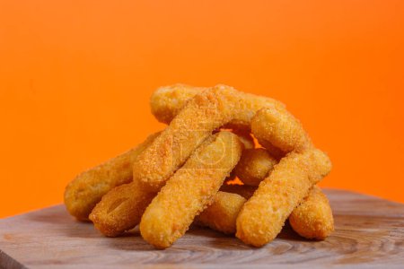 Photo for Stack of crispy mozzarella cheese sticks on a wooden board. Studio shot with orange background. Snack and comfort food concept. Design for menu, poster, and banner. - Royalty Free Image
