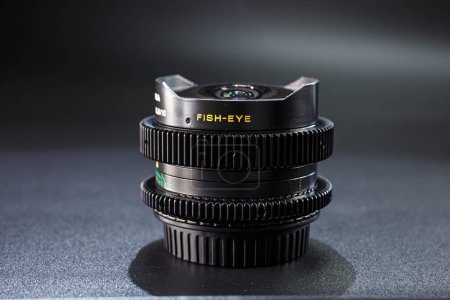Schwarzes Fischaugen-Kameraobjektiv mit Vintage-Fotoausrüstung, scharfer Gravur und hervorgehobenen, strukturierten Fokusringen vor dunklem Hintergrund.