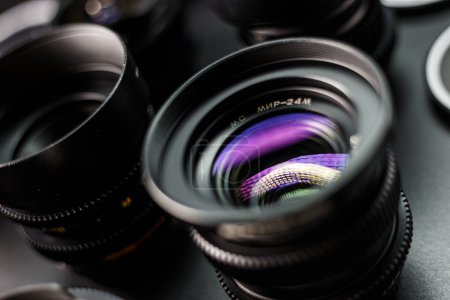 Foto de Primer plano de una lente MC vintage que muestra patrones de luz de colores, rodeada por una colección de lentes de cámara con bordes borrosos, escaparate de equipos de fotografía. - Imagen libre de derechos