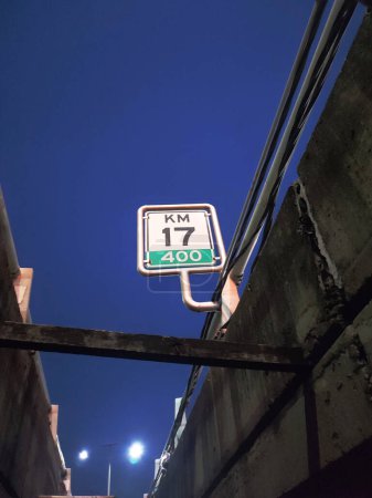 Photo for Toll road millage, Indonesian highway road sign shot from under the bridge during evening, deep blue night sky. Kilometer 17 written on the sign. Portrait photo shot from low angle perspective. - Royalty Free Image