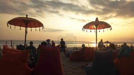Foto de Puesta de sol en la playa de La Plancha, Bali. Gente pasando el rato juntos, se sientan en bolsas de frijoles con sombrilla. - Imagen libre de derechos