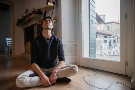 Photo for Young man sitting on the floor in meditation with crossed legs and arms. - Royalty Free Image