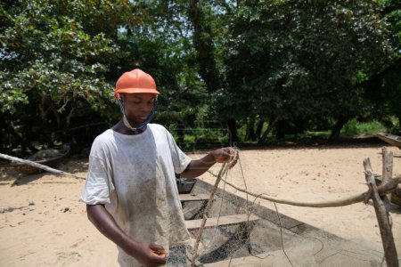 Téléchargez les photos : A young fisherman adjusts his net on his boat before a fishing session - en image libre de droit